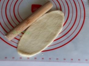 取一个中间发酵好的面团，用擀面杖擀成长椭圆形；