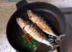 将鱼两面煎至金黄色，干红辣椒和葱碎放入锅中炒香