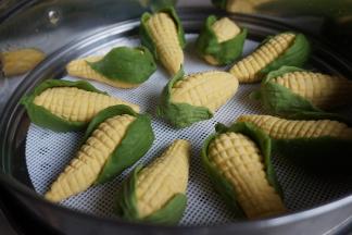 每两片叶子包住玉米底部，底部捏合在一起，搓出小尖。待锅里的水烧开后，放上蒸笼，隔水蒸10-12分钟