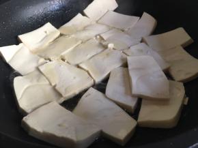 往锅中倒入稍多的食用油，食用油不宜太少，避免粘锅。油6成热后，将豆腐沿着锅边放入，并小心溅油，锅边放满后可以晃动煎锅调整空隙，当然也可以直接放入，但是一定不要太高，容易溅油以致烫伤；