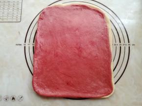 把白色面团放在底部上边，放上红曲粉面团。两个面团之间可以抹少量的水，让它们紧密地贴合在一起