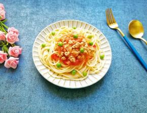 用煮过意面的水煮一些青豆，将意面盛在盘子里，浇上肉酱，撒上几颗青豆。