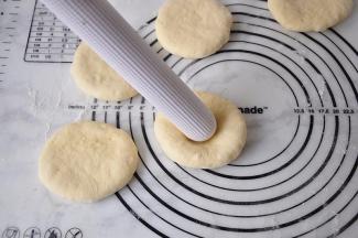 用手将面团压扁，用擀面杖的一头在面团中间捣一个深窝。