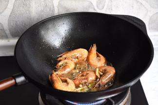 保持大火，用锅铲轻压虾头，炒出虾膏，让锅中的油脂变得红通通的，这是这个菜鲜香好吃的关键！然后放入葱段，姜丝炒匀。