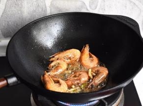 保持大火，用锅铲轻压虾头，炒出虾膏，让锅中的油脂变得红通通的，这是这个菜鲜香好吃的关键！然后放入葱段，姜丝炒匀。