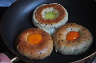 将贝果横剖开，放进淋了少许橄榄油的的平底锅中，然后将鸡蛋的蛋黄和蛋清分别放入贝果中，上半部分放蛋黄，下半部分放蛋白。注意，用的锅一定要平，放入蛋后可以轻按一会定形，不让蛋白蛋黄流下来。这里还有一点要注意，制作贝果时，中间留的洞要跟蛋黄差不多。注意，要保持小火，这样才能不糊锅，也可以适当淋一点水，盖上锅盖，这样可以促进蛋黄的凝固。