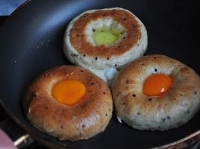 将贝果横剖开，放进淋了少许橄榄油的的平底锅中，然后将鸡蛋的蛋黄和蛋清分别放入贝果中，上半部分放蛋黄，下半部分放蛋白。注意，用的锅一定要平，放入蛋后可以轻按一会定形，不让蛋白蛋黄流下来。这里还有一点要注意，制作贝果时，中间留的洞要跟蛋黄差不多。注意，要保持小火，这样才能不糊锅，也可以适当淋一点水，盖上锅盖，这样可以促进蛋黄的凝固。