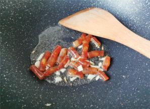 热锅倒入冷油，把蒜瓣切片放入爆香，接着小腊肠段倒入翻炒下。