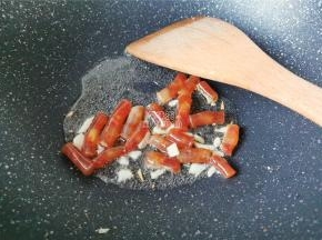 热锅倒入冷油，把蒜瓣切片放入爆香，接着小腊肠段倒入翻炒下。