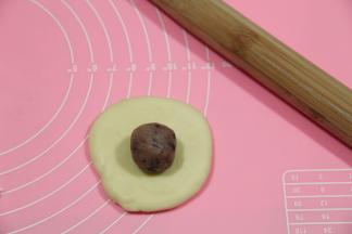 取一松弛好的面团，收口朝下，擀成圆形，翻面，放上馅料球。