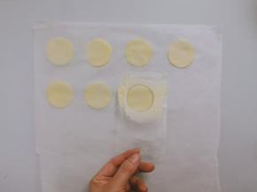 裁一张烤盘大小的油纸。将油纸放在台面上，用刮刀取少量面糊，利用塑料模板，抹平成薄薄的一层面糊，然后将纸模板提起，这样就在油纸上留下了圆形的薄面糊