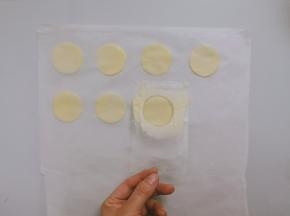 裁一张烤盘大小的油纸。将油纸放在台面上，用刮刀取少量面糊，利用塑料模板，抹平成薄薄的一层面糊，然后将纸模板提起，这样就在油纸上留下了圆形的薄面糊