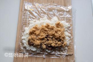 将微热的米饭铺在保鲜膜上，不要铺满，米饭铺的太满不好卷。在米饭的一头放一勺香菇酱，放适量的肉松铺开。