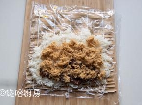 将微热的米饭铺在保鲜膜上，不要铺满，米饭铺的太满不好卷。在米饭的一头放一勺香菇酱，放适量的肉松铺开。
