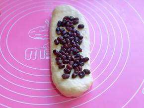 卷好的卷用擀面杖再次擀长舌状，放上蜜豆，卷起，收口朝下，依次做完。