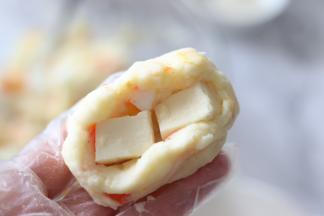 戴好一次性不粘手套，取一部分土豆泥，内部放入2块小奶酪块，封好口。