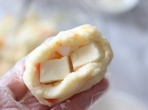 戴好一次性不粘手套，取一部分土豆泥，内部放入2块小奶酪块，封好口。
