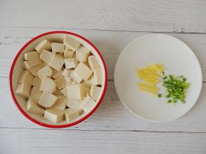 将豆腐切成大小均匀的块状，平铺在碗底，生姜切成细丝，小葱切成葱花。