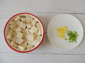 将豆腐切成大小均匀的块状，平铺在碗底，生姜切成细丝，小葱切成葱花。