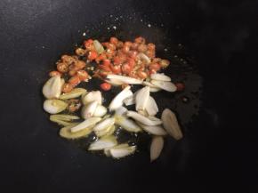 在锅中添上适量的食用油，油烧热后，放入红椒和蒜片，翻炒出香味；