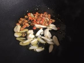 在锅中添上适量的食用油，油烧热后，放入红椒和蒜片，翻炒出香味；