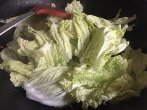 将白菜菜梗炒至稍微透明变软后，将白菜叶子滤干水份，倒入锅中，继续大火翻炒；