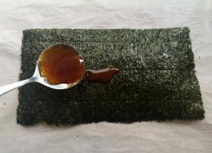 取一张海苔，用小勺子舀适量的糖浆放到海苔上，用刷子把糖浆刷均匀，边边角角也要刷