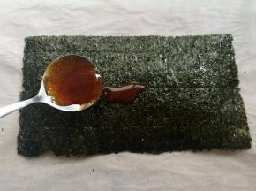 取一张海苔，用小勺子舀适量的糖浆放到海苔上，用刷子把糖浆刷均匀，边边角角也要刷