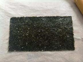 取另一张海苔，同样的在上面刷上糖浆，盖到撒了白芝麻的海苔上，用擀面杖把叠在一起的2张海苔反复擀几次，让它们贴合在一起