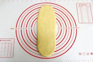 取一份松弛好的面团，用手拍扁，用擀面杖把面团擀成长舌状。