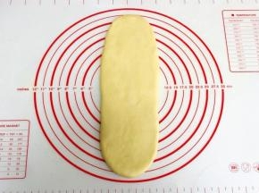 取一份松弛好的面团，用手拍扁，用擀面杖把面团擀成长舌状。