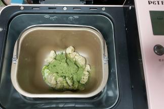 然后先把其中一块面团简单收拢成圆形，放入盆内，盖上保鲜膜进行一次发酵，另一份再次剪成小块放回面包机内，加入抹茶粉以及少许牛奶，继续启动程序。（牛奶跟抹茶粉也可以提前搅拌均匀）