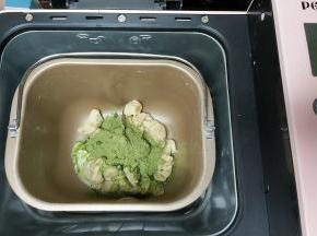 然后先把其中一块面团简单收拢成圆形，放入盆内，盖上保鲜膜进行一次发酵，另一份再次剪成小块放回面包机内，加入抹茶粉以及少许牛奶，继续启动程序。（牛奶跟抹茶粉也可以提前搅拌均匀）