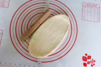 取一个中间发酵好的面团，用擀面杖擀成长椭圆形；