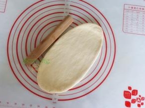 取一个中间发酵好的面团，用擀面杖擀成长椭圆形；