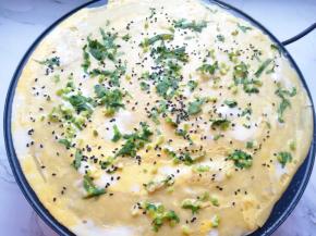 舀一勺面糊倒在煎饼果子机的中间位置，用竹蜻蜓转圈抹开，鸡蛋提前打散，将蛋液均匀的倒在煎饼上面，撒上熟黑芝麻和香菜碎（因为一个人操作，动作要迅速，所以中间步骤没有来得及拍照）。