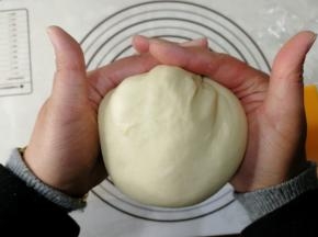 取出面团，不要使劲拉，用软刮板，铲出来。然后拿掉打面钩。双手握住面团，向身体外侧折叠2-3次收圆。手法如图。