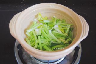 万土锅的底部倒入少许油，晃匀锅底，把芹菜叶蒜苗的茎摆入锅内。