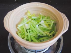 万土锅的底部倒入少许油，晃匀锅底，把芹菜叶蒜苗的茎摆入锅内。