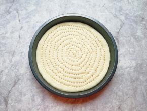 擀成一张和模具大小一致的面饼，放进披萨盘里，用叉子扎满小孔，防止饼皮在烤制的过程中中间凸起。