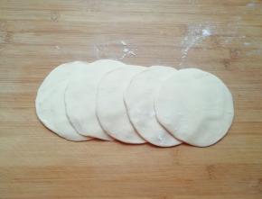 将小剂子压扁，擀成中间稍厚边缘薄的包子皮。