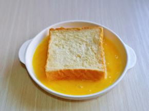 取一片吐司，放入蛋液中，吐司片均匀裹上蛋液。