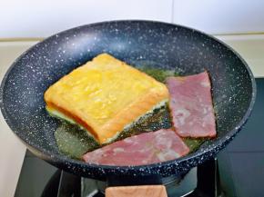将裹好蛋液的吐司片，放入平底锅中，再把培根加入一起煎，小火煎至两面金黄即可。