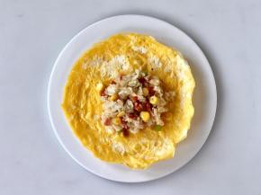 把适量的炒饭舀入蛋皮中间，边缘捏褶把饭包起，收口用焯过的黄瓜皮切成细条扎起来。