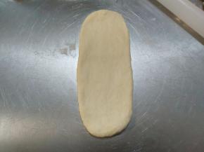 取出一个松弛好的面团，用擀面杖自中间分别向上向下擀开，成长条状。