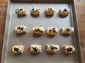 用刷子把手抓饼香肠卷上刷上适量的生鸡蛋黄，撒上一些黑芝麻