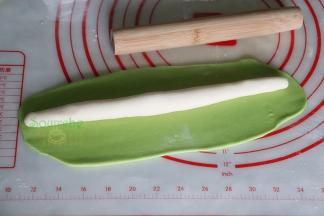 取一个菠菜小面团用擀面杖擀成长方形的面皮，另外一个白菜面团揉搓长条。用菠菜汁面团包裹白面团，再次揉搓成长条。