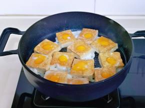 待底部煎至金黄时将豆腐翻面，这时把鹌鹑蛋磕入圆圈中，保持小火煎至。