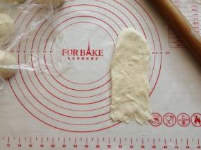 用擀面棍把松弛过的面团擀成长条形，顺便把气泡压破，其中一条短边用手指压薄