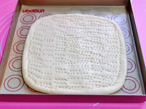 大面团擀成正方形，放入垫有油纸的烤盘中，同样叉出不规则的洞洞。